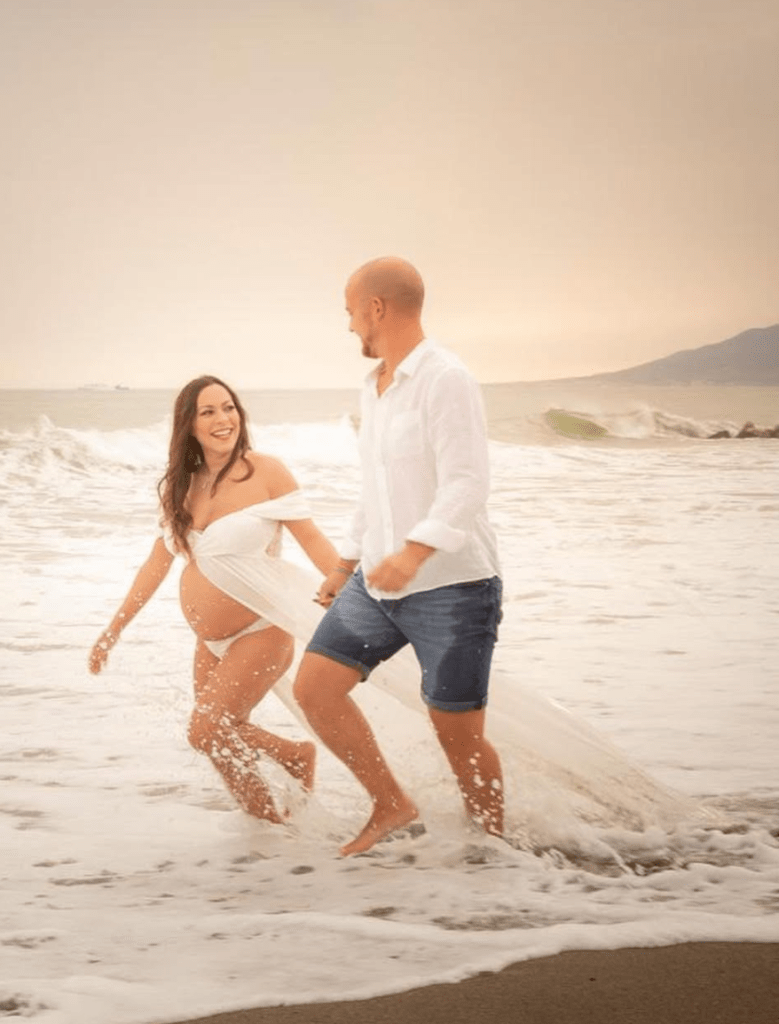 pareja corriendo y jugando en el mar durante sesión de embarazo en la playa con estilo natural